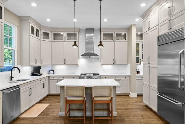 kitchen with wall chimney exhaust hood, appliances with stainless steel finishes, light countertops, and a sink