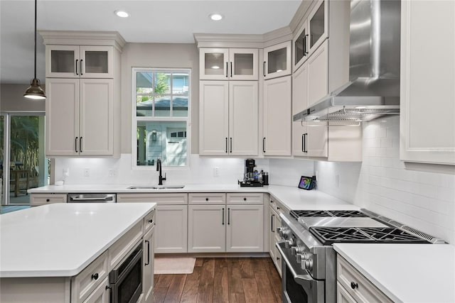 kitchen featuring stainless steel appliances, dark wood-style flooring, a sink, light countertops, and wall chimney exhaust hood