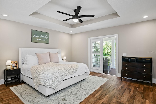 bedroom with access to outside, dark wood-type flooring, and a raised ceiling