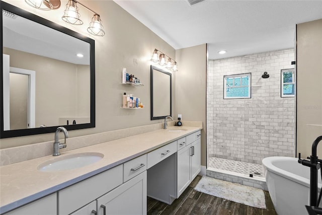 full bath featuring double vanity, a sink, a tile shower, and wood finished floors