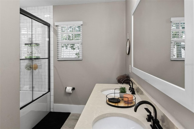 bathroom featuring double vanity, shower / bath combination with glass door, baseboards, and a sink