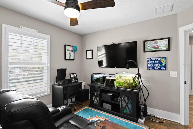 living room with ceiling fan, a textured ceiling, wood finished floors, visible vents, and baseboards