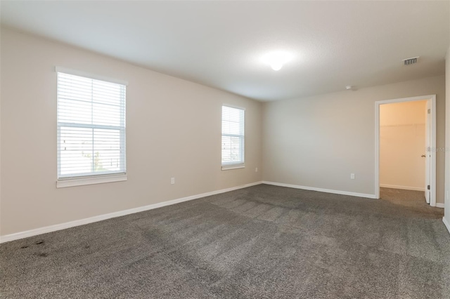 empty room featuring dark colored carpet, visible vents, and baseboards