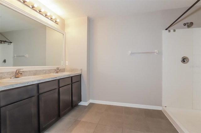 full bath with double vanity, a shower, a sink, and baseboards