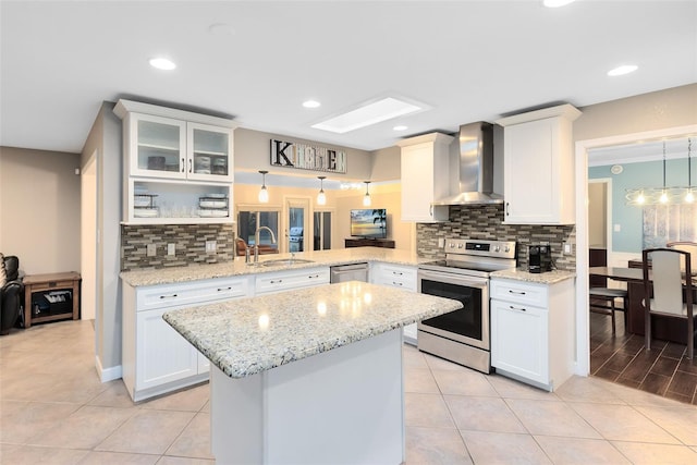 kitchen featuring a peninsula, a sink, glass insert cabinets, appliances with stainless steel finishes, and wall chimney exhaust hood