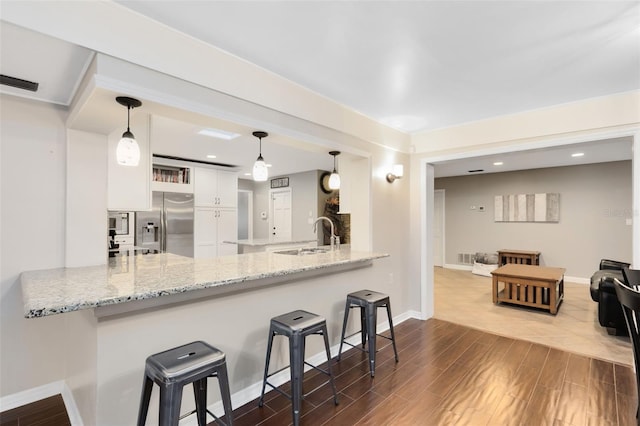 kitchen with visible vents, a sink, stainless steel fridge, a peninsula, and white cabinets