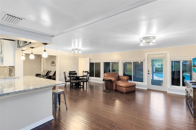 interior space featuring visible vents, light stone countertops, dark wood finished floors, a kitchen bar, and a sink