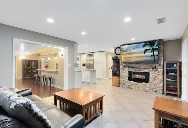 living room featuring a stone fireplace, light tile patterned flooring, recessed lighting, and visible vents