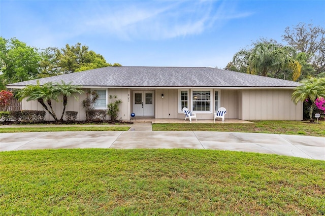 ranch-style house with board and batten siding, a shingled roof, and a front yard