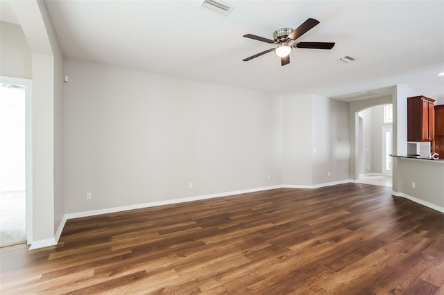 unfurnished living room with dark wood-style floors, visible vents, and arched walkways