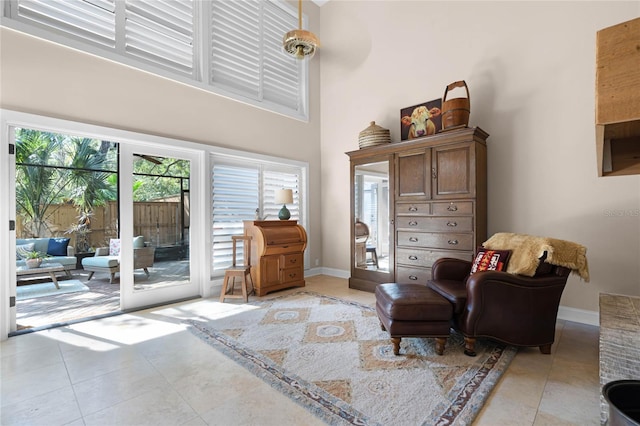 living area with light tile patterned floors, a towering ceiling, and baseboards