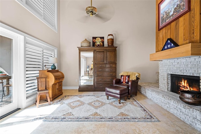 sitting room featuring ceiling fan, tile patterned flooring, a fireplace, a towering ceiling, and baseboards