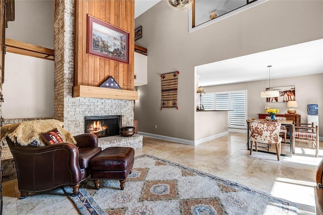 tiled living area with a brick fireplace, a towering ceiling, and baseboards