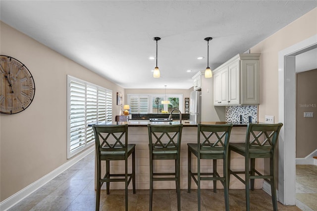 kitchen featuring a peninsula, baseboards, a kitchen breakfast bar, freestanding refrigerator, and tasteful backsplash