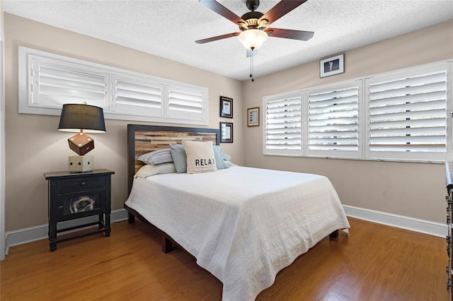 bedroom with a textured ceiling, wood finished floors, and baseboards