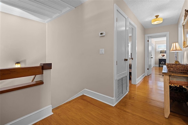 hallway with visible vents, a textured ceiling, an upstairs landing, light wood-type flooring, and baseboards