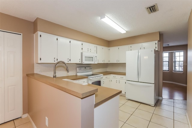 kitchen with white appliances, visible vents, white cabinets, a peninsula, and light countertops