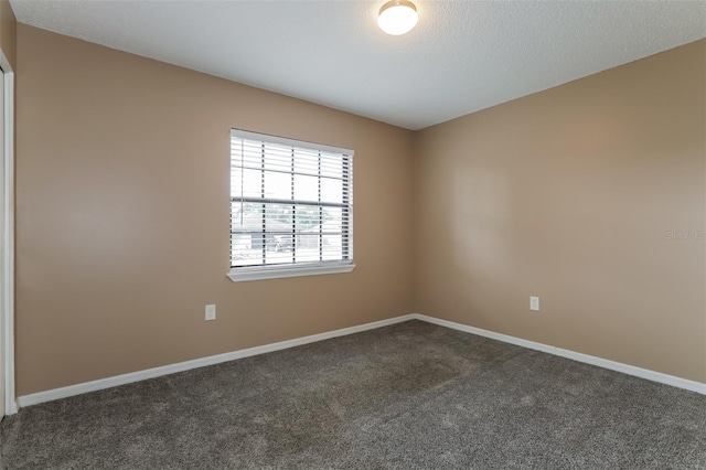 spare room featuring dark carpet, a textured ceiling, and baseboards