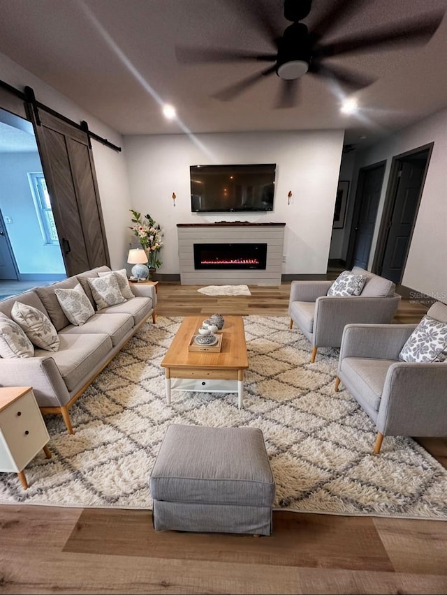 living room featuring recessed lighting, a barn door, ceiling fan, wood finished floors, and a warm lit fireplace