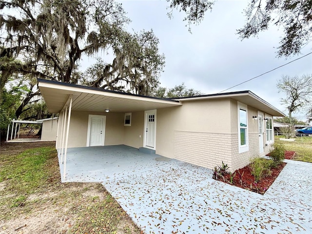 view of front of property with a carport, brick siding, driveway, and stucco siding