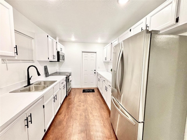 kitchen with stainless steel appliances, light countertops, white cabinetry, and a sink