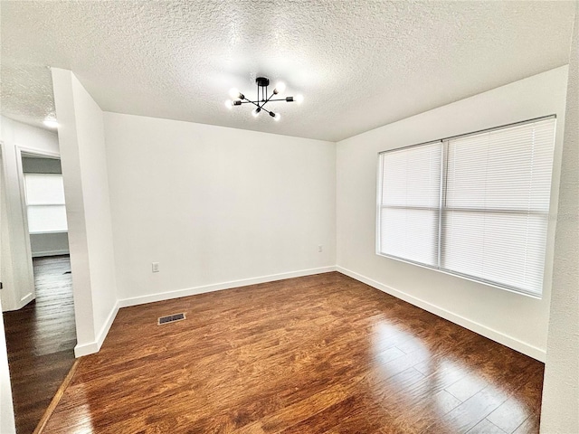 unfurnished room featuring baseboards, visible vents, dark wood finished floors, a textured ceiling, and a notable chandelier