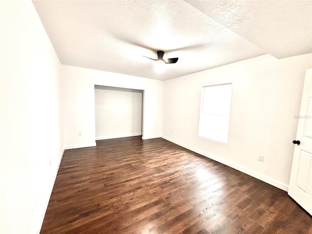 spare room with a textured ceiling, dark wood finished floors, and baseboards