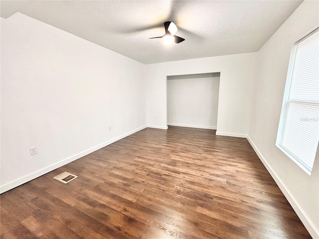 spare room featuring baseboards, visible vents, ceiling fan, dark wood-style flooring, and a textured ceiling