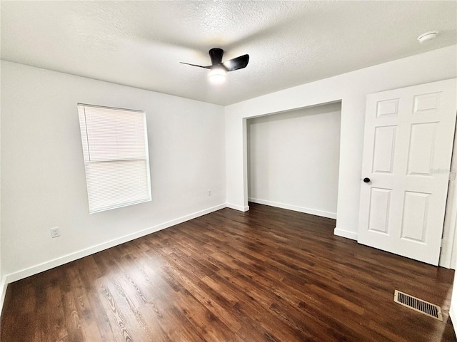 unfurnished bedroom with dark wood-style flooring, visible vents, a textured ceiling, and baseboards