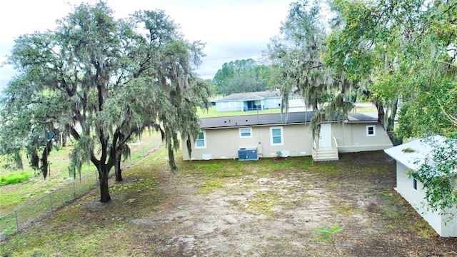 rear view of house with entry steps, central AC unit, and fence