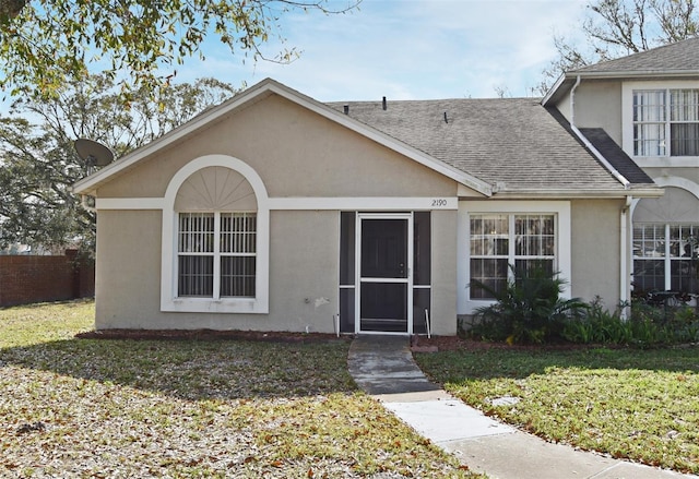 view of front facade featuring a front yard, roof with shingles, and stucco siding