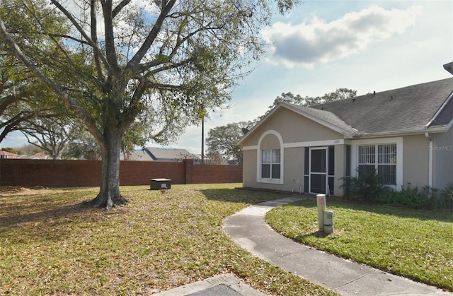 view of property exterior with a shingled roof, stucco siding, fence, and a lawn