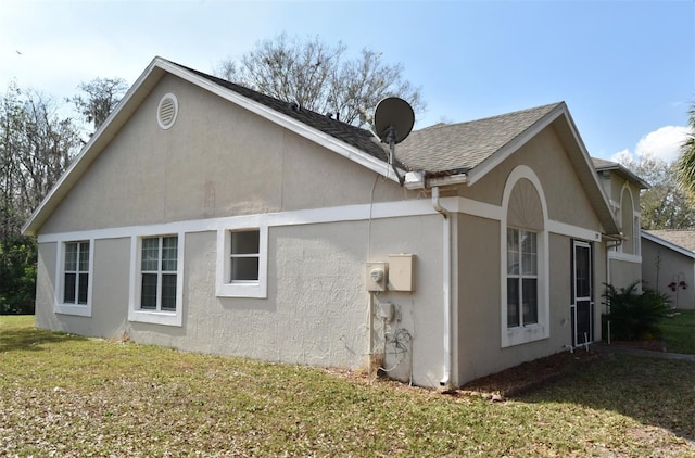 rear view of house with a yard, roof with shingles, and stucco siding