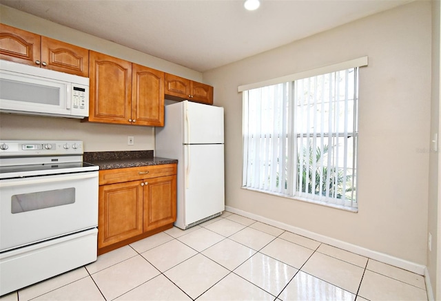 kitchen with brown cabinetry, dark countertops, white appliances, and light tile patterned floors