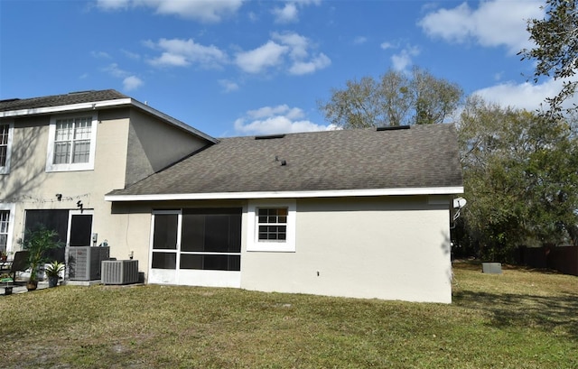 rear view of property with central AC, a sunroom, a yard, roof with shingles, and stucco siding