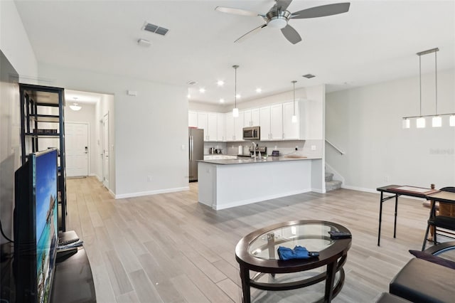 living room with light wood-style floors, stairway, visible vents, and a ceiling fan