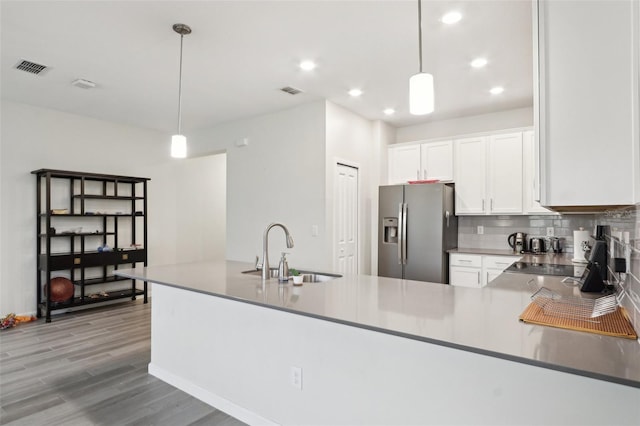 kitchen with wood finished floors, a sink, white cabinets, stainless steel refrigerator with ice dispenser, and tasteful backsplash