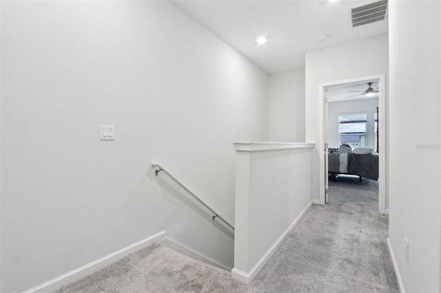 hallway featuring carpet flooring, visible vents, and an upstairs landing