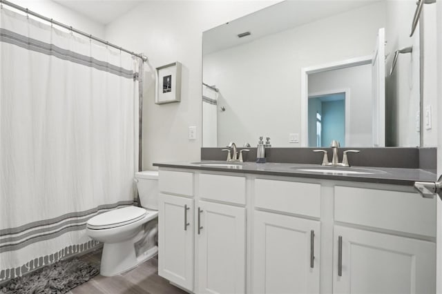 full bath featuring double vanity, a sink, toilet, and wood finished floors