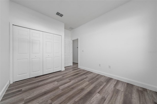 unfurnished bedroom featuring dark wood-style floors, baseboards, visible vents, and a closet