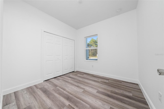 unfurnished bedroom with light wood-style flooring, baseboards, and a closet