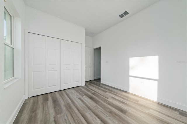 unfurnished bedroom with light wood-type flooring, baseboards, visible vents, and a closet