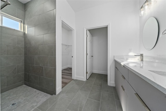 full bathroom with double vanity, baseboards, tiled shower, a spacious closet, and a sink