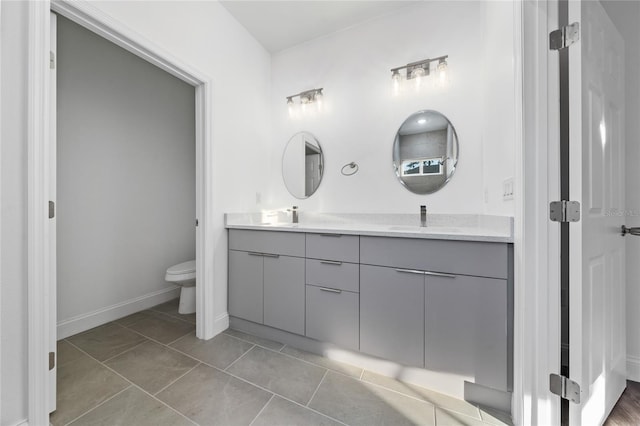 bathroom featuring toilet, double vanity, a sink, and tile patterned floors