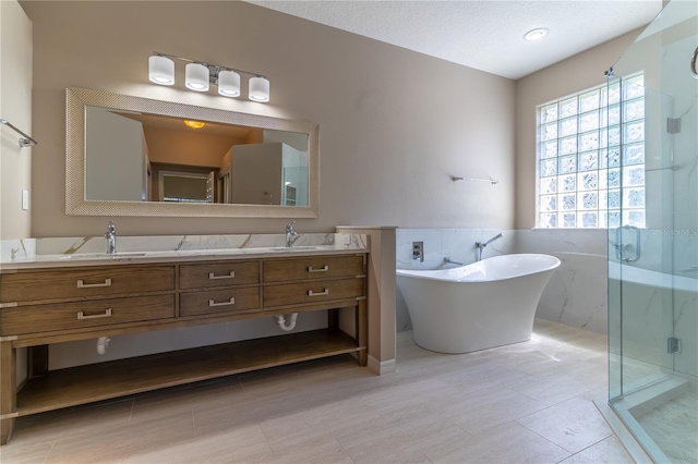 bathroom with a textured ceiling, double vanity, a marble finish shower, a sink, and a freestanding bath