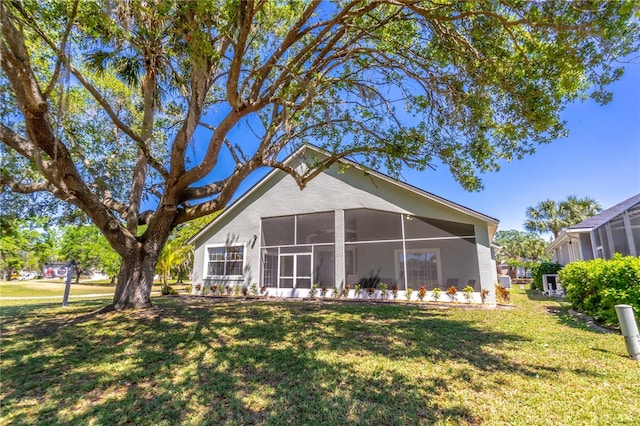 rear view of property with a lawn, a sunroom, and stucco siding