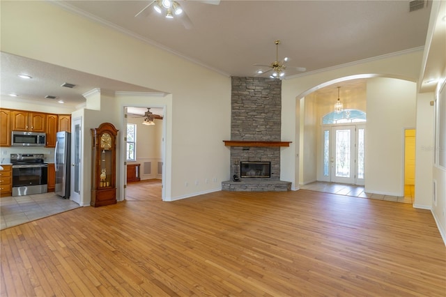 unfurnished living room with a stone fireplace, light wood-type flooring, arched walkways, and a ceiling fan