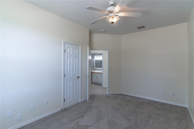 empty room featuring a textured ceiling, visible vents, baseboards, a ceiling fan, and light colored carpet