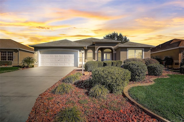 prairie-style home featuring driveway, a garage, roof with shingles, a front lawn, and stucco siding