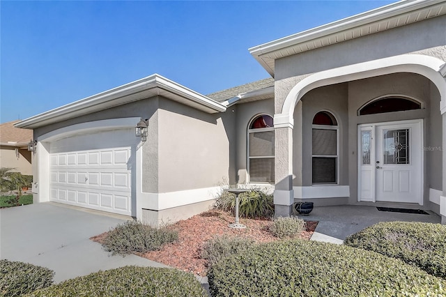 property entrance with driveway, an attached garage, and stucco siding